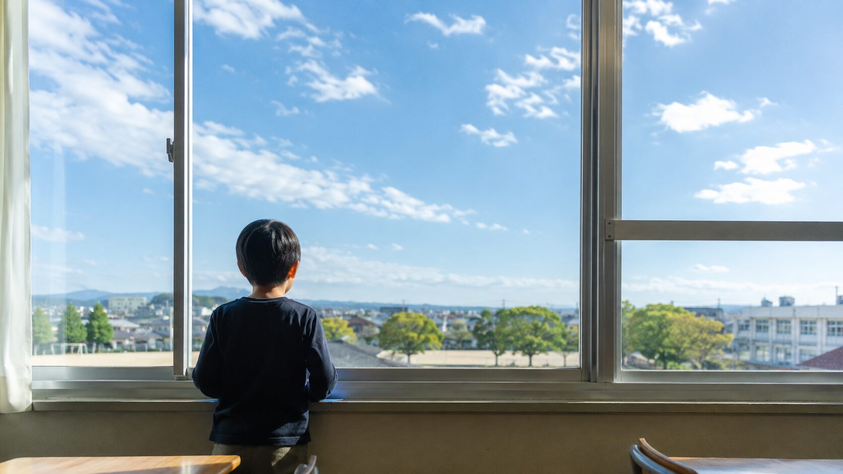 転校先の新しい教室の窓から外を眺める子ども