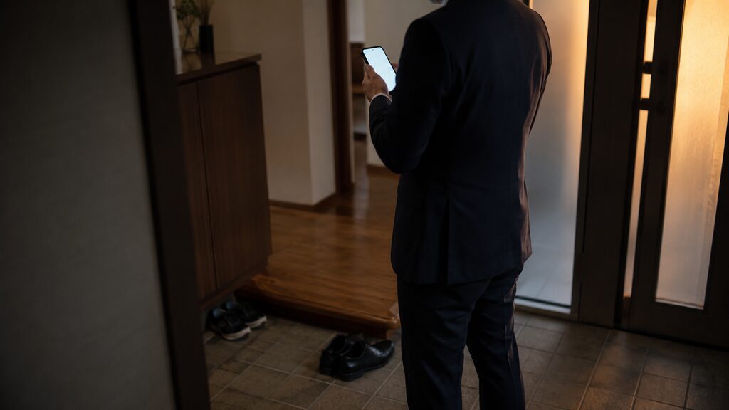 夕方の玄関でスマートフォンを見つめる男性の後ろ姿